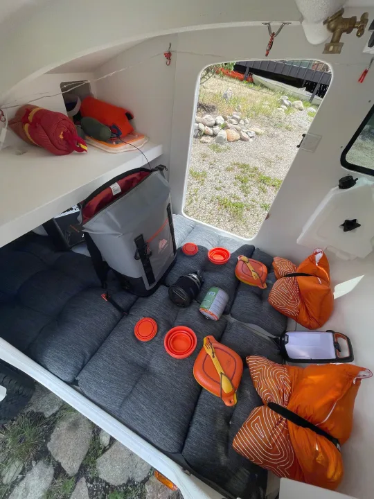 Compact RV rental interior showing organized camping gear: sleeping bags, cooler, and dishes ready for adventure.. Other Other 2022