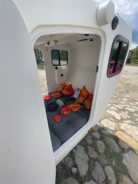 Cozy interior of a small RV rental, featuring a gray mattress, orange pillows, and camping gear for a comfortable road trip.. Other Other 2022