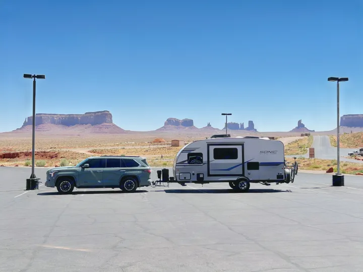 A grey SUV towing an RV rental travel trailer in a Monument Valley desert parking lot under a bright blue sky.. Sonic Lite 2022