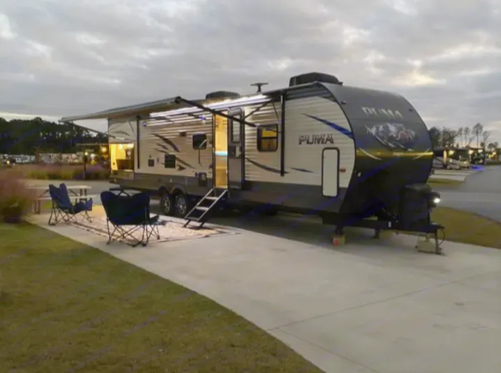 Night falls over a well-equipped RV rental, a Puma travel trailer with bright interior and extended awning. Perfect for campsite relaxation.. Palomino Puma 31DBTS 2020