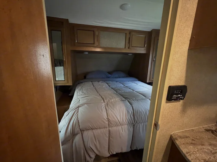 Experience comfort in this RV rental's cozy bedroom. It features a bed with overhead cabinets & a side window.. Coachmen 273BHS 2019