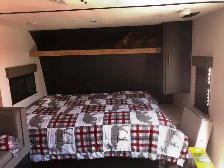 Cozy RV rental bedroom with patterned bedding, a cat napping on the shelf, window blinds, and cabinet storage.. Keystone RV Springdale 2022