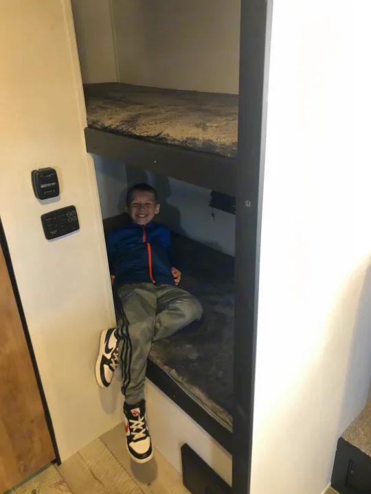 A young boy smiles from the comfortable bunk beds inside an RV rental, perfect for family adventures.. Keystone RV Springdale 2022