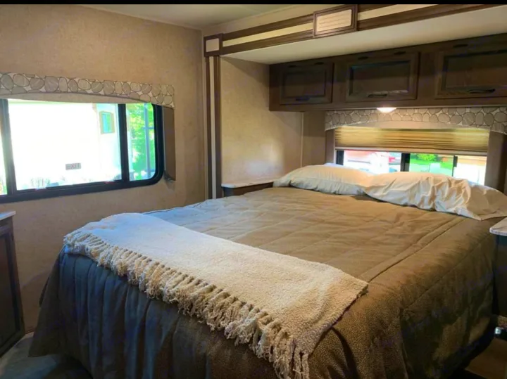 Cozy RV rental bedroom with a large bed, side windows, and overhead cabinets, offering comfort for your travels.. Chevy 4500 2019