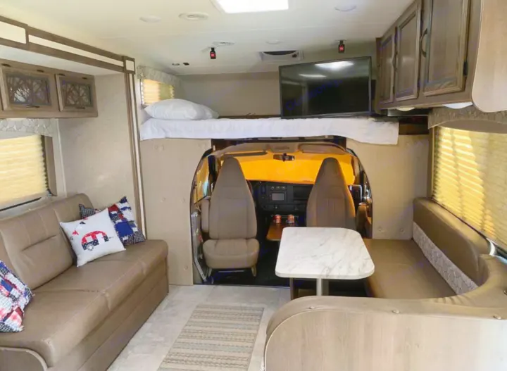 Spacious RV rental interior featuring a comfortable living area with a couch, dinette, and an overhead bed above the driver's cab.. Chevy 4500 2019