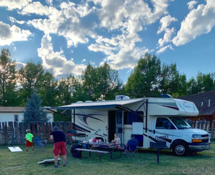A family enjoys an RV rental trip, with kids playing cornhole and others relaxing by the camper's awning.. Chevy 4500 2019