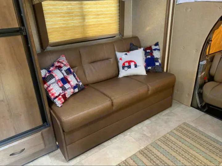 Cozy RV rental interior with a brown sofa and decorative pillows, offering a comfortable living space.. Chevy 4500 2019