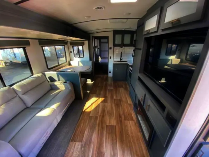 Spacious rv rental interior with a light sofa, dinette, modern kitchen, and entertainment center with TV.. Keystone RV Bullet Premier Ultra Lite 2022