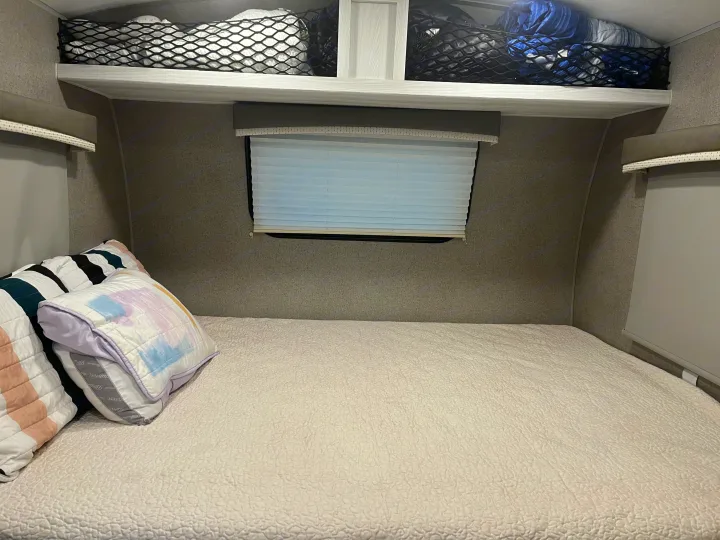 Inside this RV rental bedroom: a quilted bed, overhead storage nets with items, and window blinds for privacy.. Forest River Rockwood Geo Pro 2020