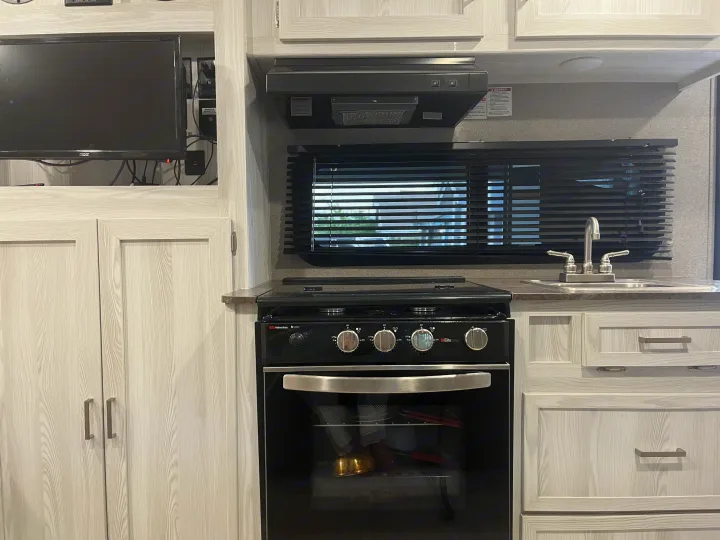 This RV rental showcases its functional kitchen: stove, oven, sink, ample cabinets, and a television.. Forest River Rockwood Geo Pro 2020