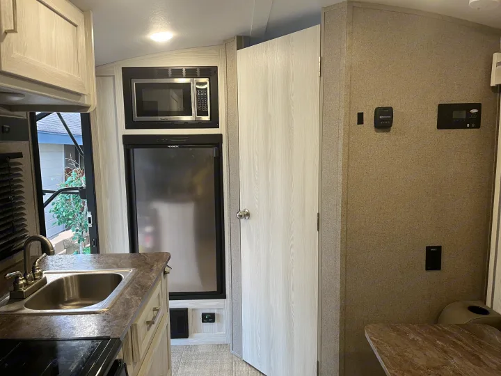 Compact and functional RV interior, showing kitchen with sink, microwave, fridge, and wall controls. Ideal for rv rental adventures.. Forest River Rockwood Geo Pro 2020