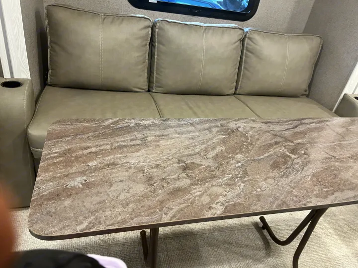 Inside an RV rental: a neutral-toned sofa with three cushions, built-in cup holder, and a practical marbled table.. Forest River Rockwood Geo Pro 2020