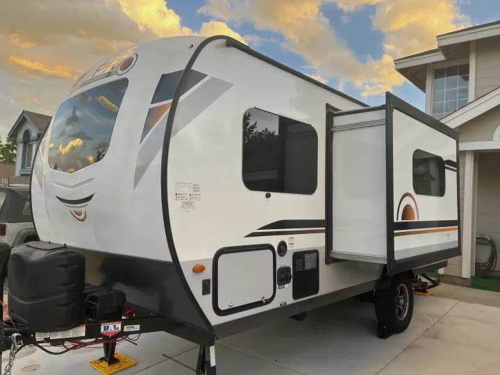 White travel trailer RV rental with a slide-out section, parked on a driveway under a cloudy sky, ready for adventure.. Forest River Rockwood Geo Pro 2020