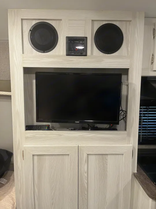 RV rental entertainment center with TV, speakers, Furrion unit, and cabinets in light woodgrain.. Forest River Rockwood Geo Pro 2020