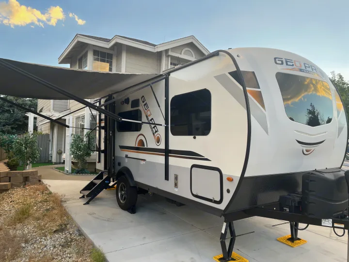 White and gray Geo Pro travel trailer RV rental with its awning extended, parked on a concrete driveway.. Forest River Rockwood Geo Pro 2020
