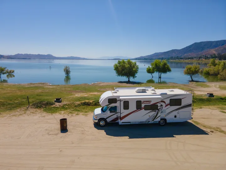 A white Coleman RV rental parked lakeside, offering stunning views of mountains across the water. Ideal for camping.. Thor Coleman 2023