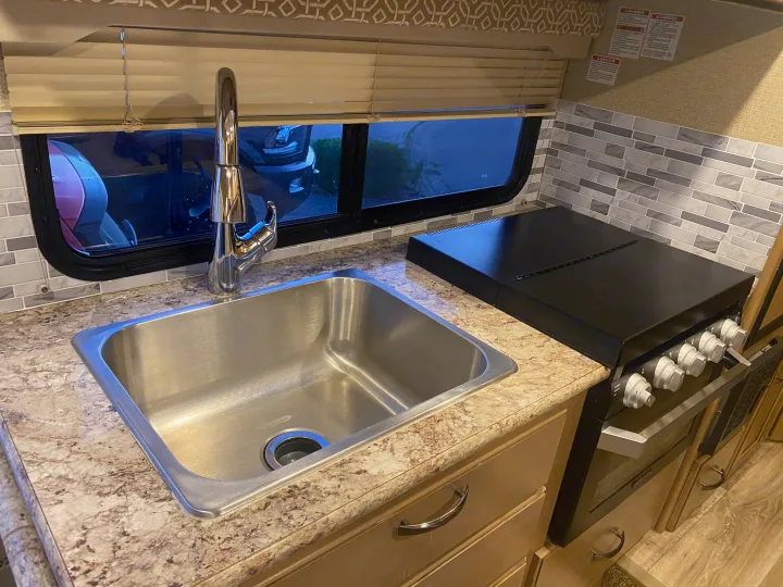 RV rental kitchen: stainless steel sink, black stove, patterned countertop, and tiled backsplash.. Thor Freedom Elite 2019