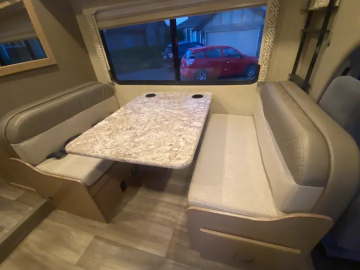 RV rental dinette with comfortable bench seating, a speckled table, and a window view of a house & red car.. Thor Freedom Elite 2019