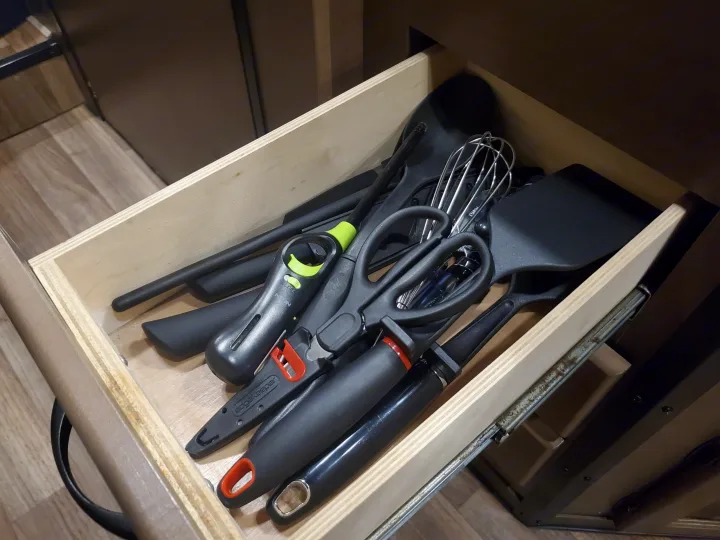 An RV rental kitchen drawer holds black spatulas, whisk, kitchen shears, a lighter, and knife sharpener, neatly organized.. Thor Majestic 2019