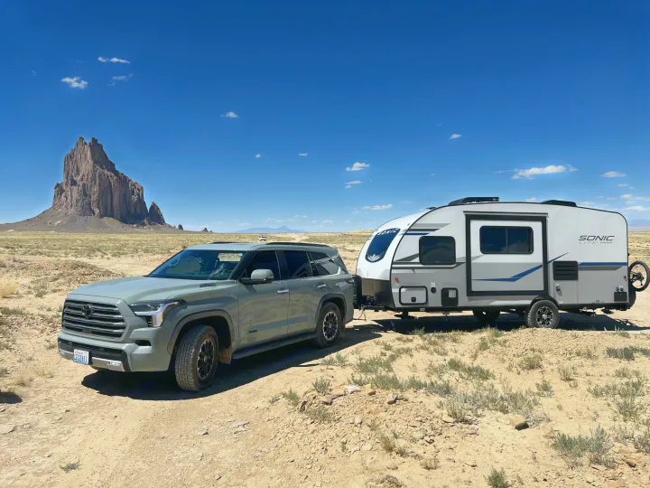 Grey SUV towing a white RV rental travel trailer on a desert road. Majestic Shiprock formation in background, sunny sky.. Sonic Lite 2022