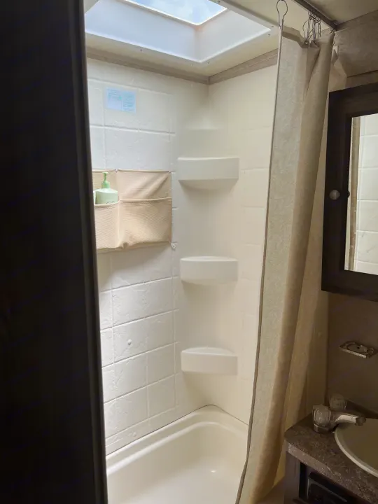 Clean RV rental shower/bathroom with skylight, shower curtain, sink vanity, and hanging organizer. Compact & functional.. Forest River Rockwood Mini Lite 2017