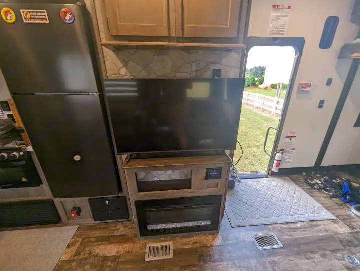 Cozy RV rental interior: fridge, TV, fireplace, and an open door revealing a grassy outdoor view.. Forest River Cherokee Wolf Pack Toy Hauler 2022