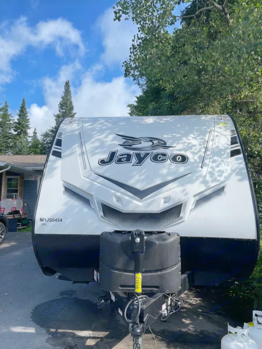 White Jayco travel trailer RV rental, front view. Parked outdoors with propane tanks visible.. Jayco Jay Feather 2021