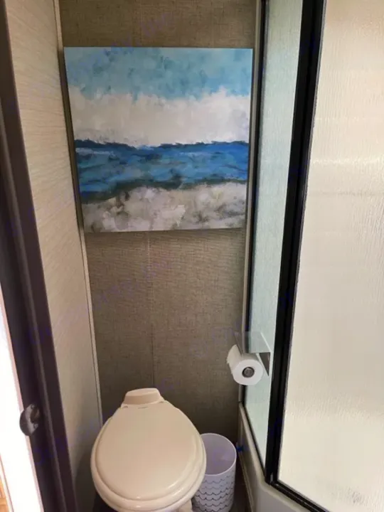 This compact RV rental bathroom features a toilet, toilet paper holder, and abstract wall art.. Keystone RV Bullet Ultra Lite 2018