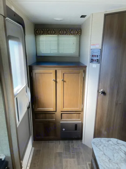 Modern RV rental interior featuring a compact kitchen with wood cabinets, a control panel, and a window with blinds.. Keystone RV Bullet Ultra Lite 2018