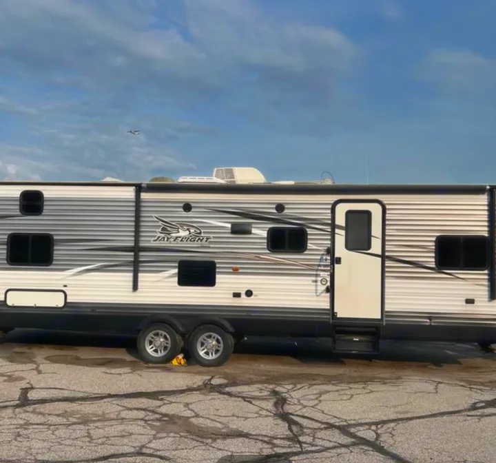 Experience comfort in this Jay Flight travel trailer, available for RV rental. Full side view parked on cracked asphalt.. Jayco Jay Flight 2016
