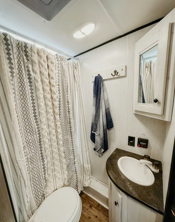 Clean RV rental bathroom showcasing a stylish patterned shower curtain, toilet, sink vanity, and mirrored cabinet. Well-equipped for travel.. Heartland RVs Trail Runner 2022