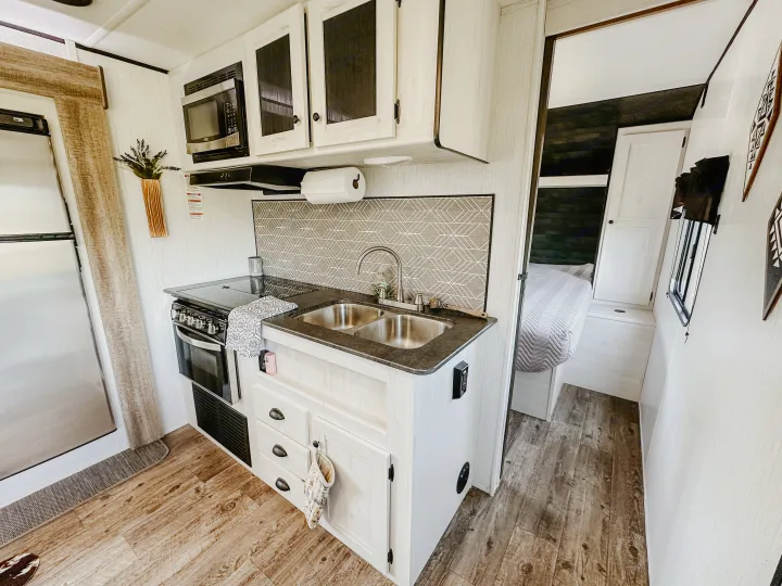 Modern RV rental interior: kitchen with stove, microwave, and sink, leading to a tidy bedroom.. Heartland RVs Trail Runner 2022