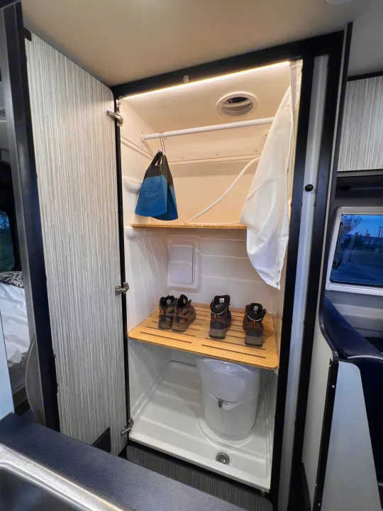 An RV rental's clever wet bath design features a toilet, shower, and multi-use wooden shelf holding boots & flippers.. Winnebago Revel 2023