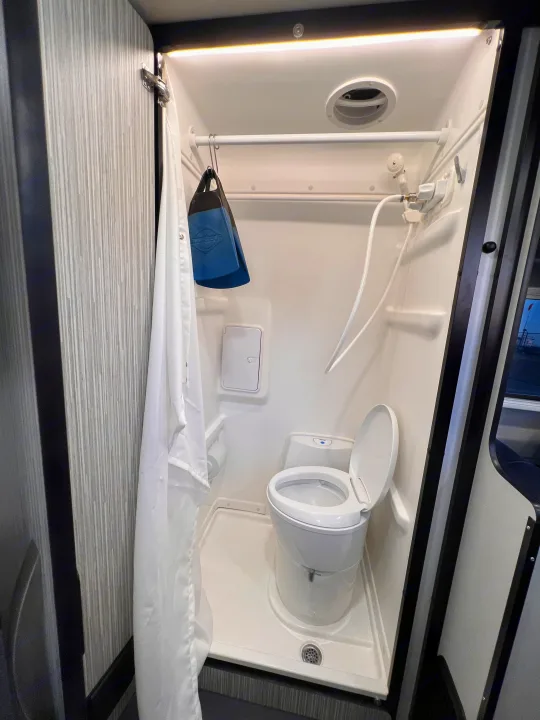 Compact RV rental wet bath featuring a toilet, handheld shower, and overhead vent for comfort.. Winnebago Revel 2023