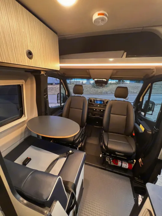 Inside a modern RV rental: Comfortable swivel seats, dinette table, and overhead storage create a functional and inviting interior for travel.. Winnebago Revel 2023