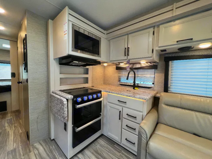 Modern RV rental kitchen showcasing a microwave, oven, sink, and light cabinetry, perfect for comfortable travel.. Thor Freedom Elite 2023
