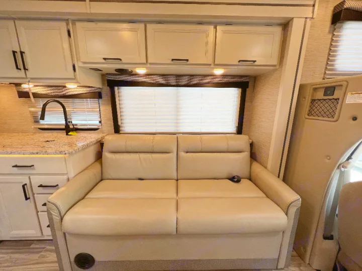 Modern RV rental interior with bright kitchen, counter, black faucet, and comfortable beige sofa, perfect for road trips.. Thor Freedom Elite 2023