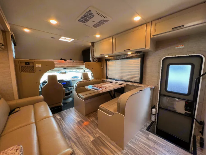 Spacious RV rental interior featuring a dinette, sofa, overhead bunk, and driver's cab view.. Thor Freedom Elite 2023