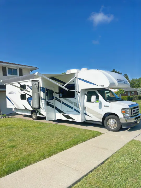 White Thor Freedom Elite RV rental, a Class C motorhome, parked on a driveway with slide-out and awning open. Travel ready!. Thor Freedom Elite 2023