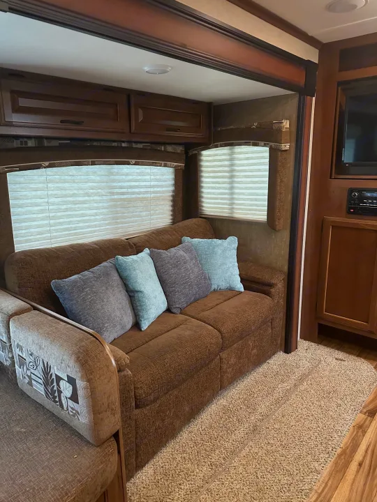 RV rental interior: A cozy living area featuring a brown sofa, light blue pillows, blinds, and wood cabinetry.. Jayco Jay Flight 2016