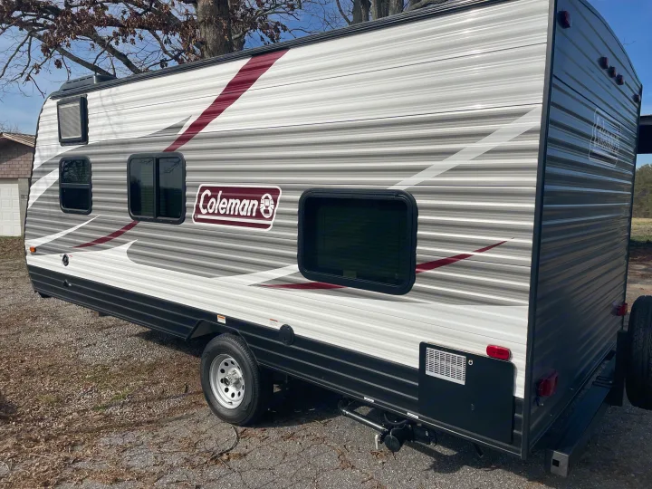 Side view of a grey Coleman travel trailer, an ideal RV rental, parked outdoors on gravel.. Dutchmen Coleman Lantern LT 2019