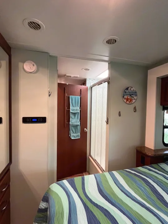 RV rental interior: cozy bedroom with striped bed, leading to bathroom door with towels, and shower stall. Features ceiling vents.. Thor Four Winds 2015