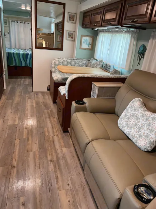 Cozy RV rental interior with a light wood-look floor, brown dinette, beige recliners, and bright bedroom.. Thor Four Winds 2015