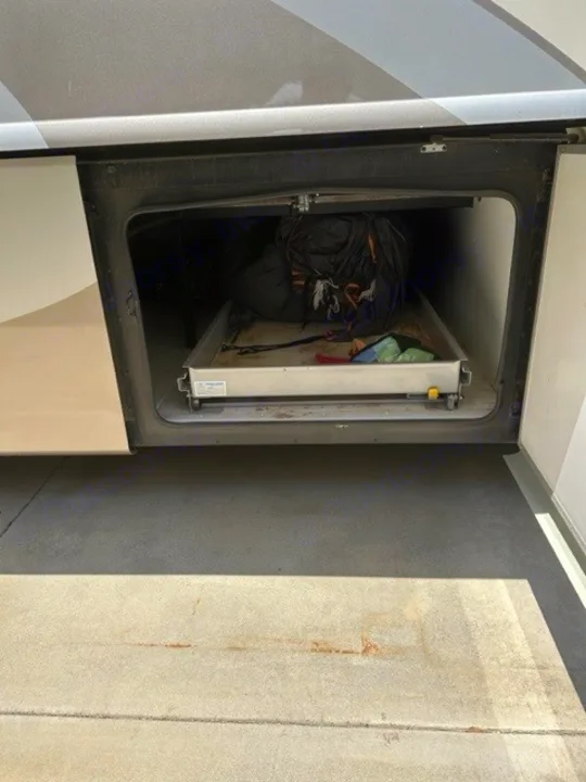 Open RV rental side storage compartment reveals a pull-out tray with camping gear, ready for travel on concrete.. Holiday Rambler Endeavor 2017