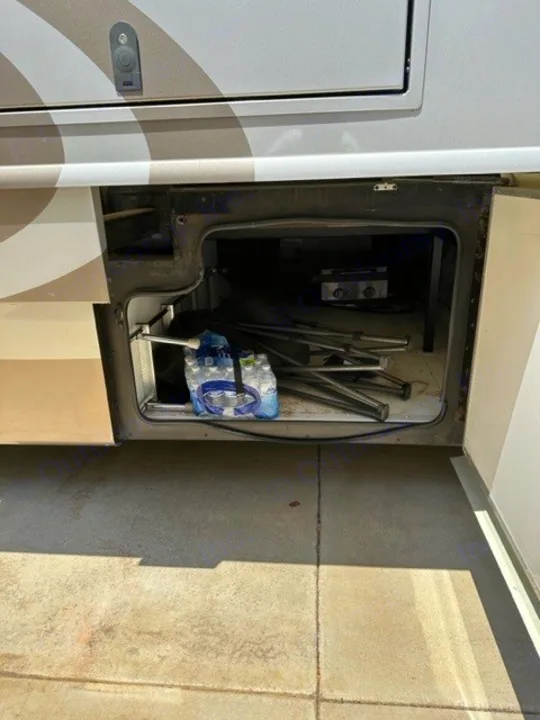 RV rental's open exterior storage bay reveals bottled water, folded chairs, and a grill, ready for your trip.. Holiday Rambler Endeavor 2017
