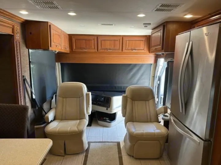 Experience comfort in our RV rental! Front view of the cabin, showing cream captain's seats, wood cabinets, and full-size fridge.. Holiday Rambler Endeavor 2017
