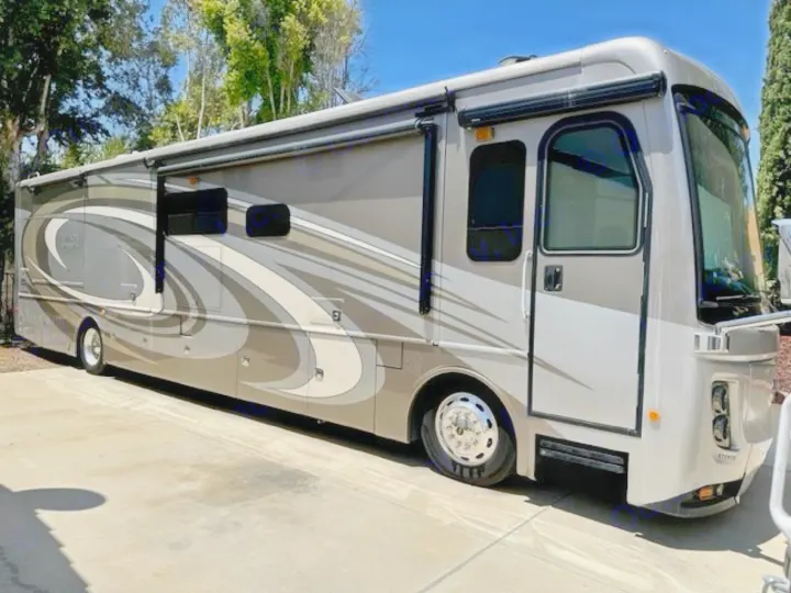 Spacious tan & grey Class A RV, parked on a driveway. Consider this well-maintained motorhome for your RV rental.. Holiday Rambler Endeavor 2017