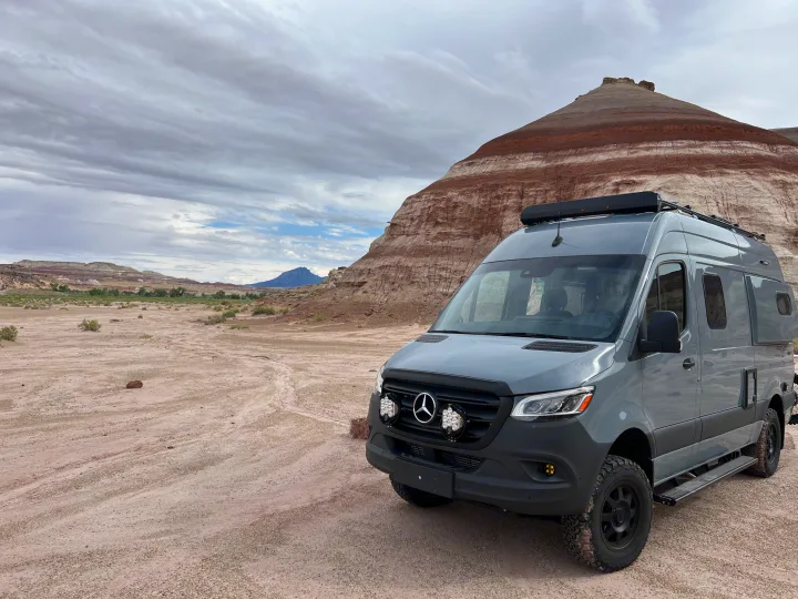 Gray Mercedes Sprinter camper van, ideal for your next rv rental, parked on a dirt road in a desert landscape.. Winnebago Revel 2023