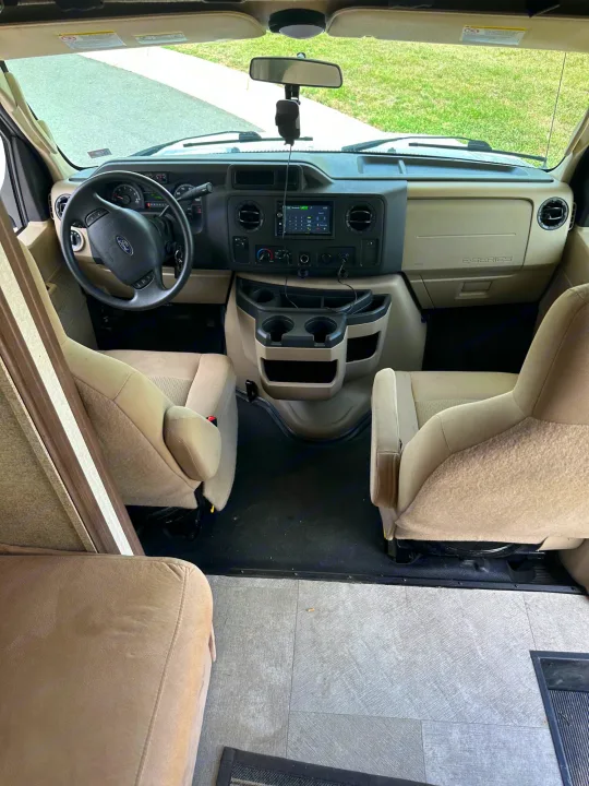 Inside an RV rental: looking towards the spacious front cockpit with comfortable tan seats, steering wheel, and dashboard.. Forest River Coachmen Freelander 2018