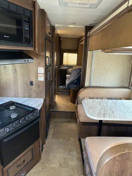 Spacious RV rental interior featuring a full kitchen, dining booth, and rear bedroom area, ideal for travel.. Forest River Coachmen Freelander 2018